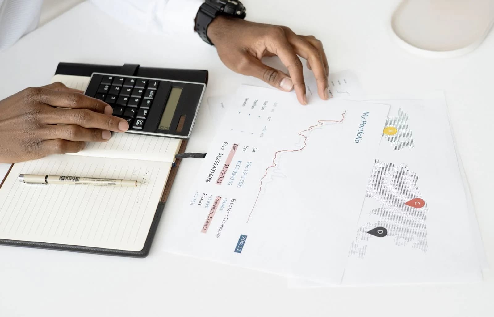 Hands reviewing printed charts with a calculator and notebook